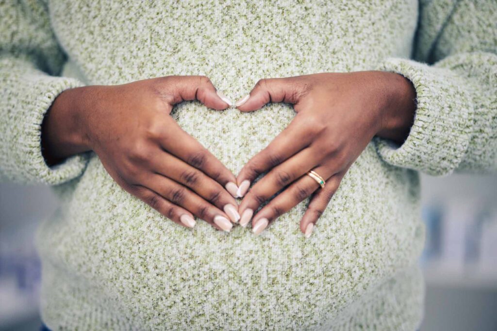 Woman in jumper making a heart sign over baby bump